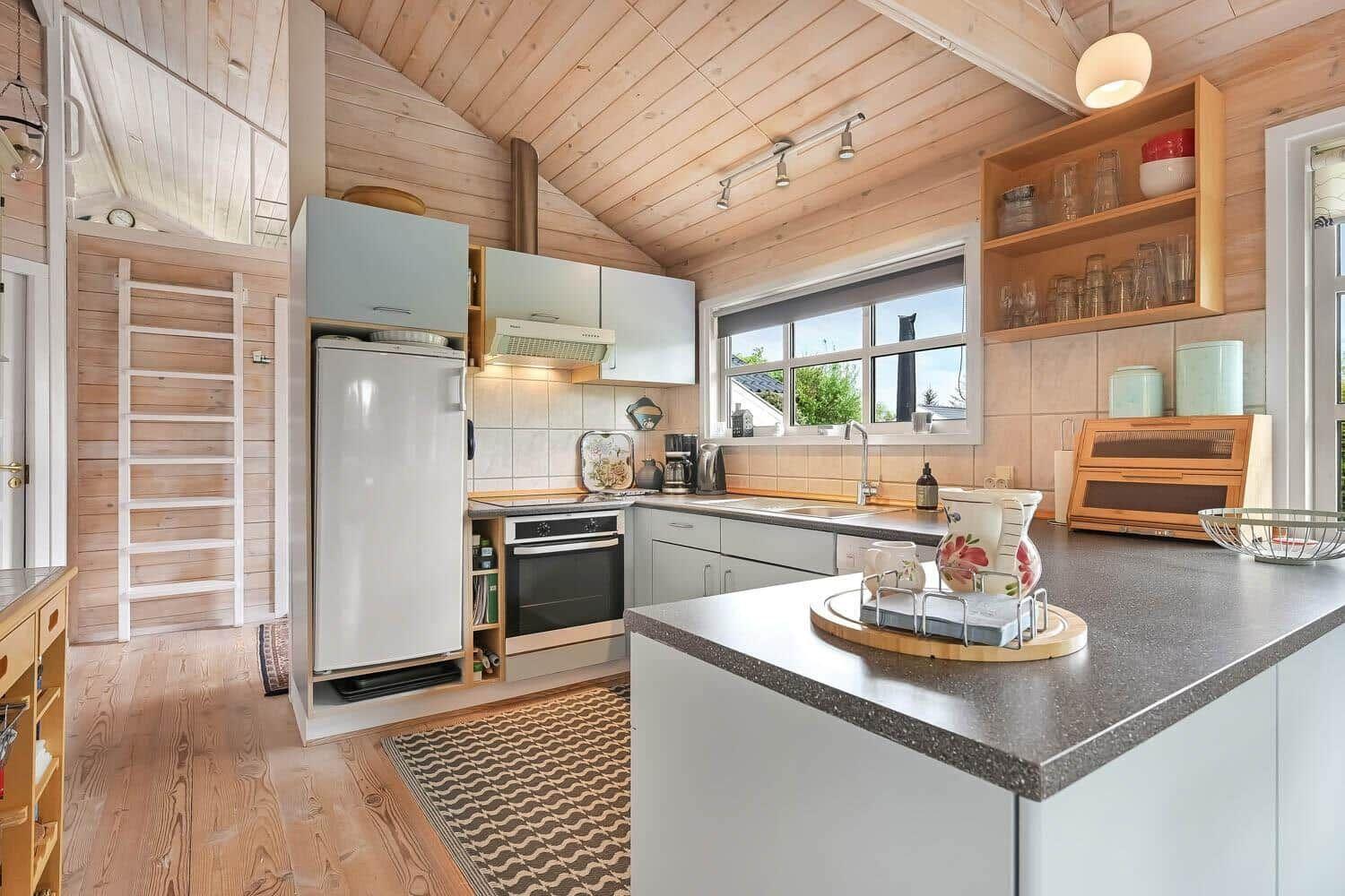 Küche mit Holzwand, Kühlschrank, Herd und Fenster.
