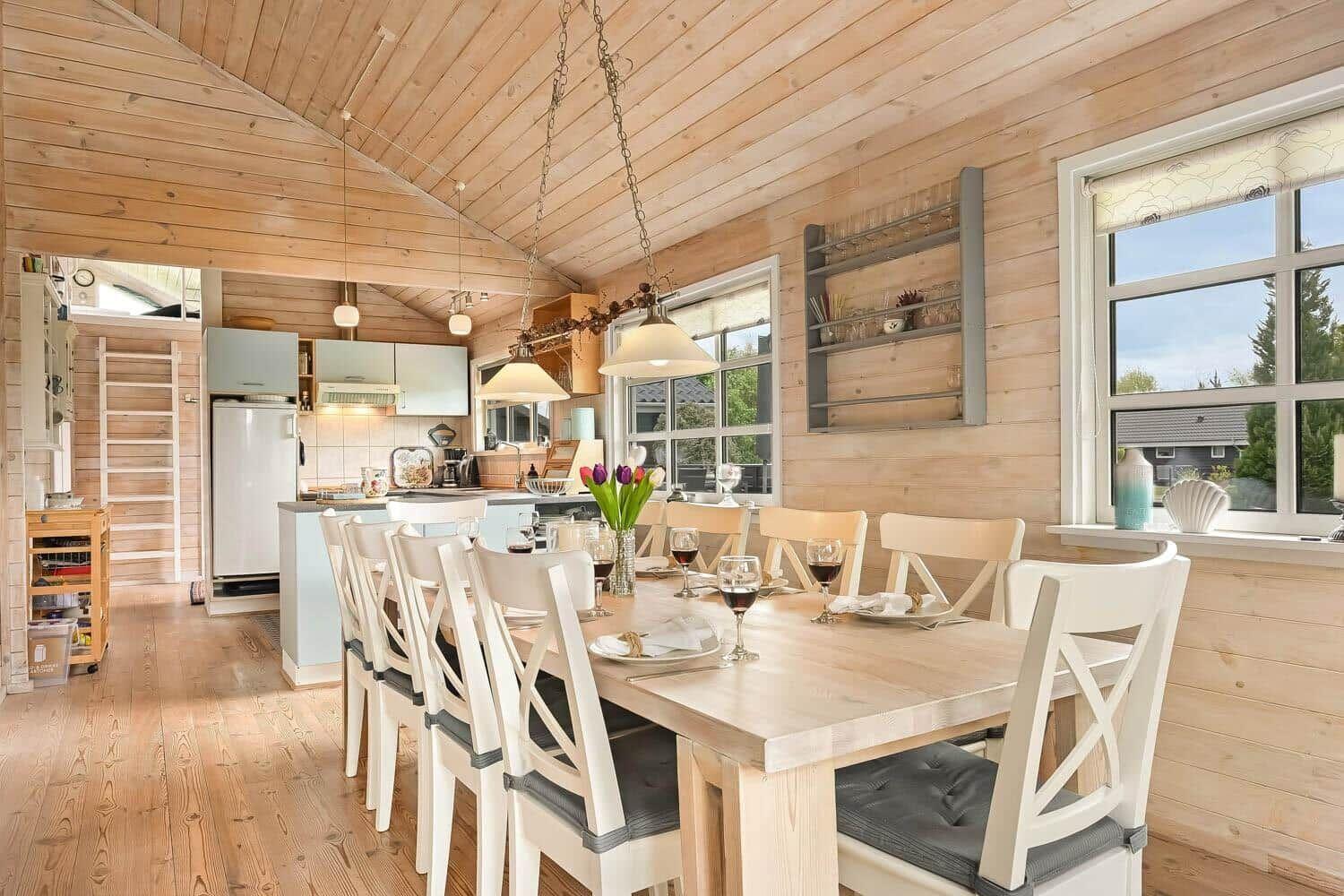 Essbereich mit Tisch und Stühlen. Küche im Hintergrund. Holzwände und -decke.