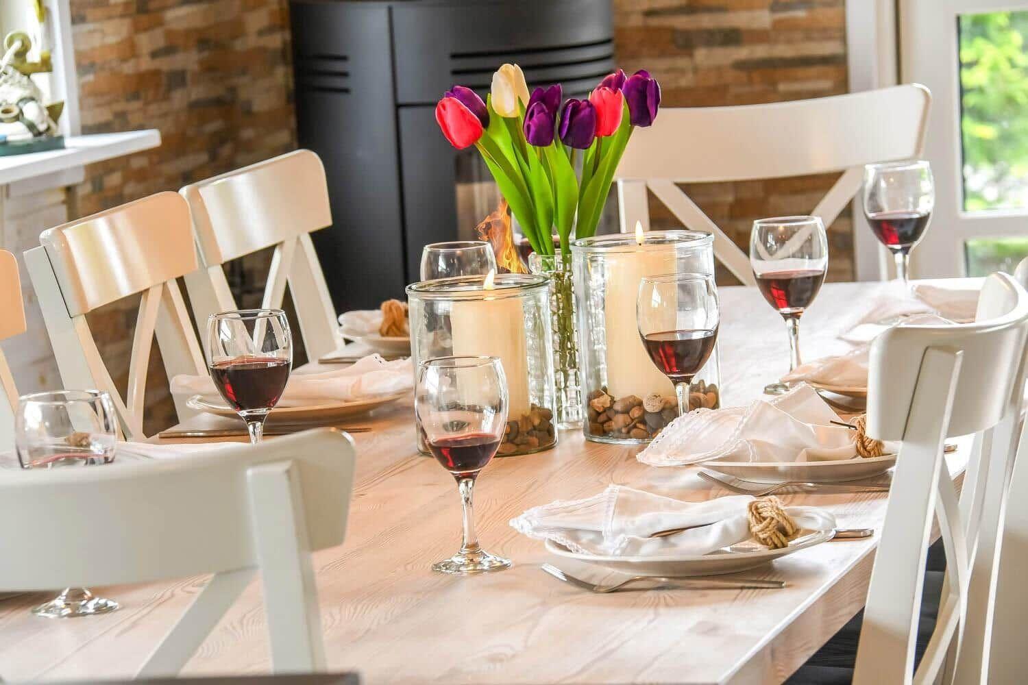 Esstisch mit weißen Stühlen, Blumen und Kerzen. Im Hintergrund steht ein Kamin.