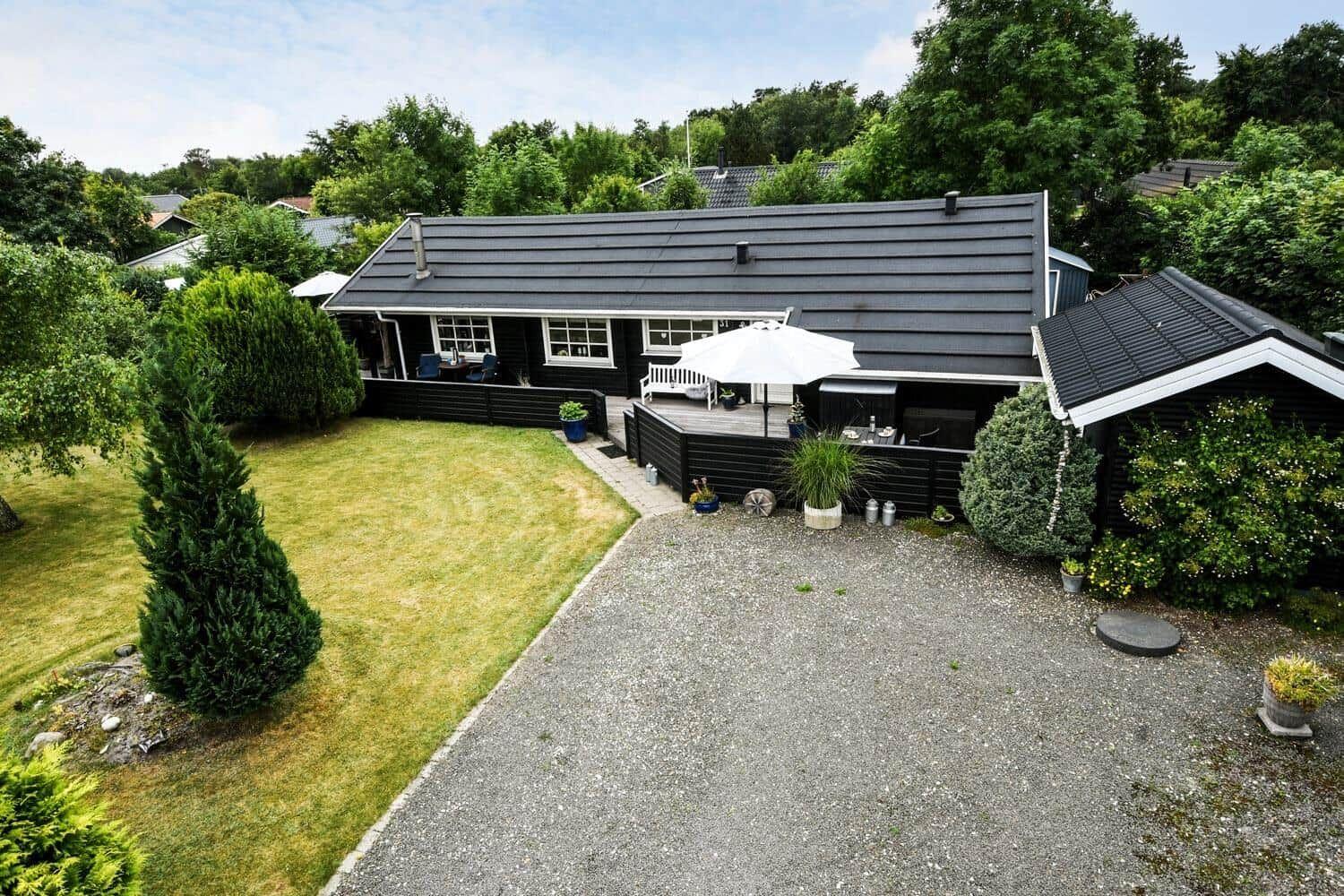 Schwarzes Haus mit Terrasse, Grill und Garten. Grasfläche und Kiesweg.