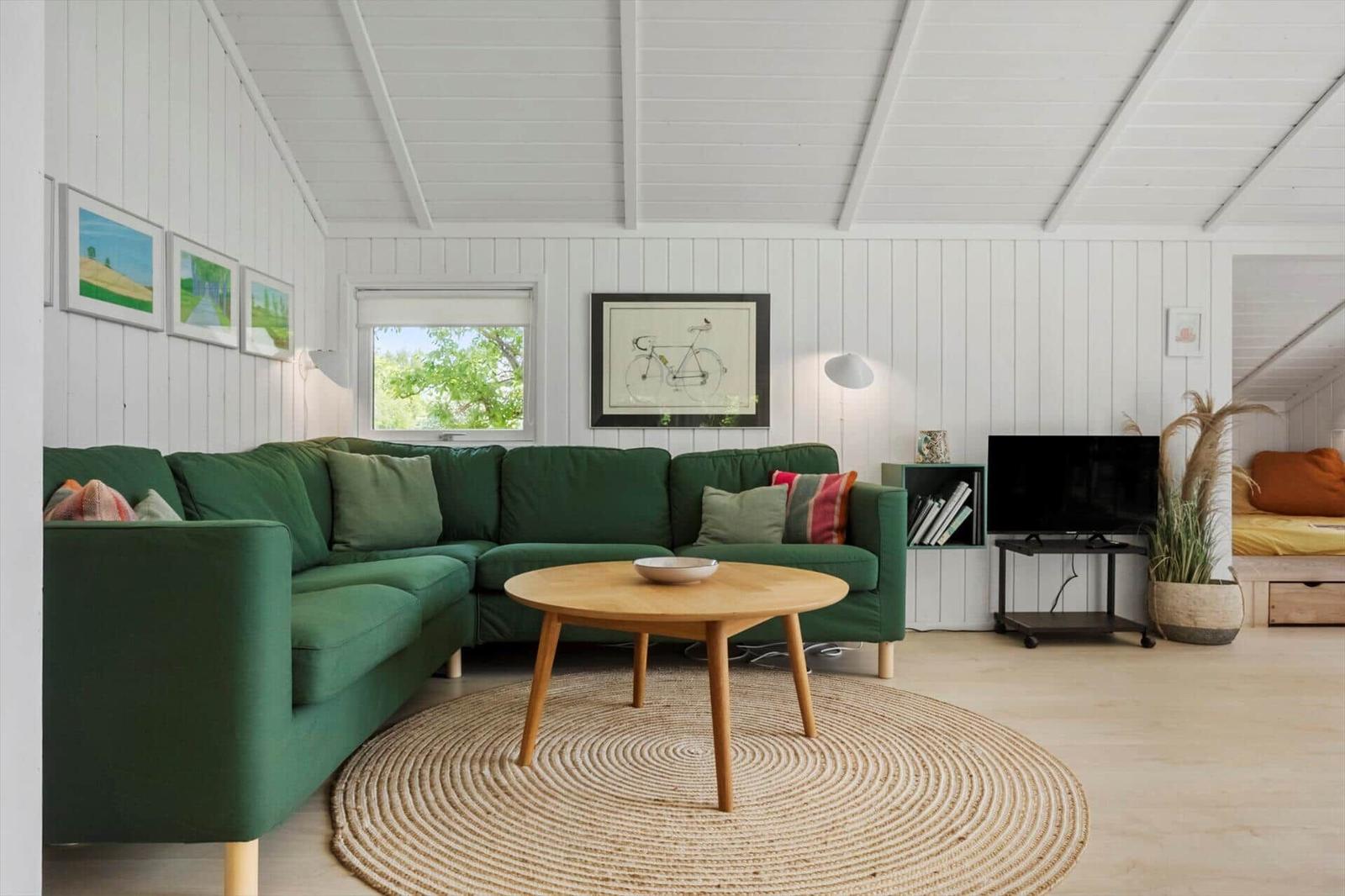Ein Wohnzimmer mit grünem Sofa, runden Teppich und Fernseher.