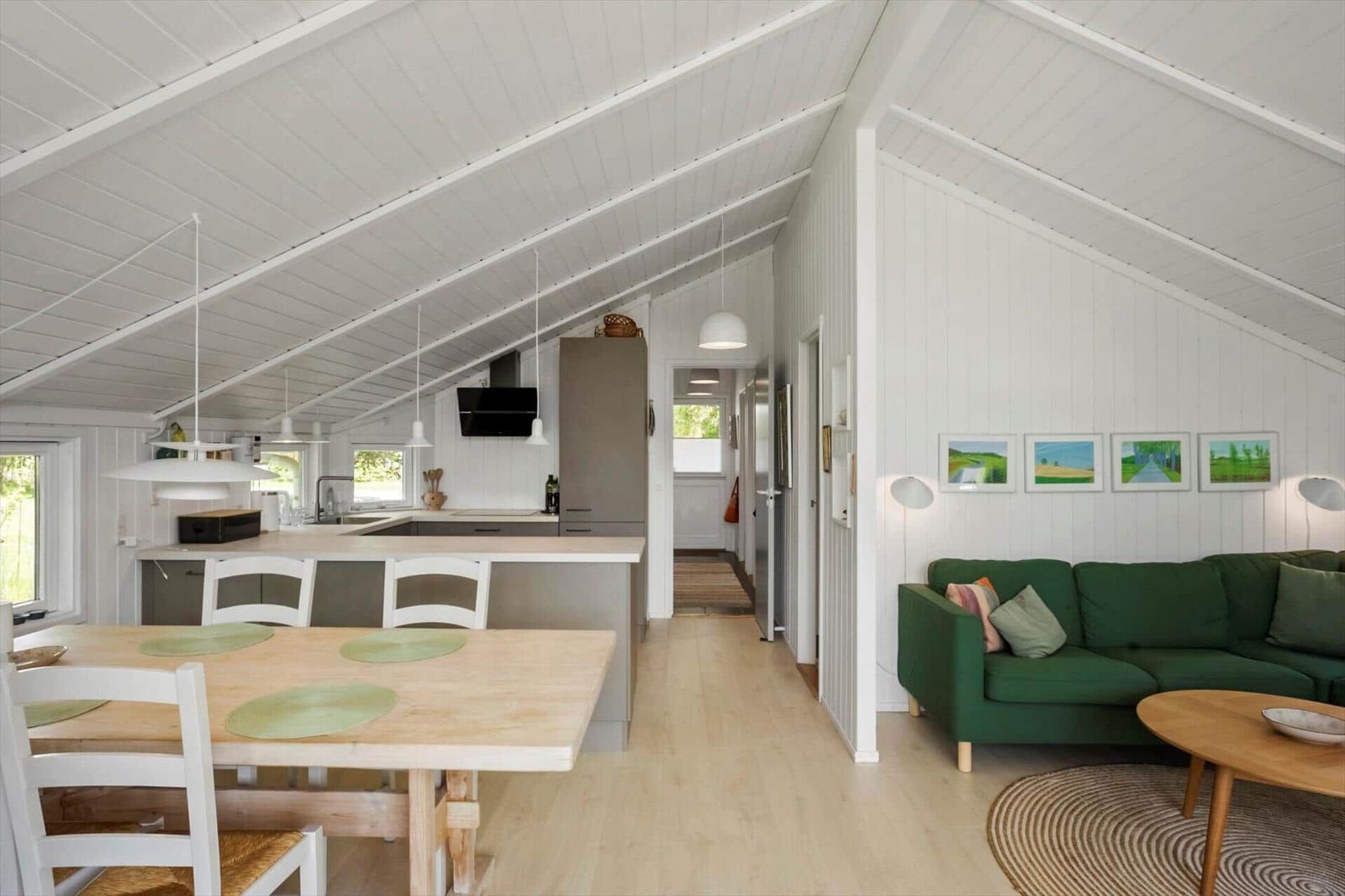 Wohn- und Essbereich mit grünem Sofa, Holztisch und weißer Küche unter schrägen Dachdecken.