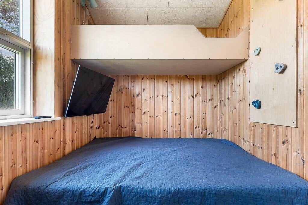 A bedroom with a bed, wall-mounted TV, and climbing wall on the wall.