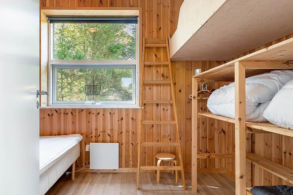 Room with wooden walls, bunk bed, window, and ladder.