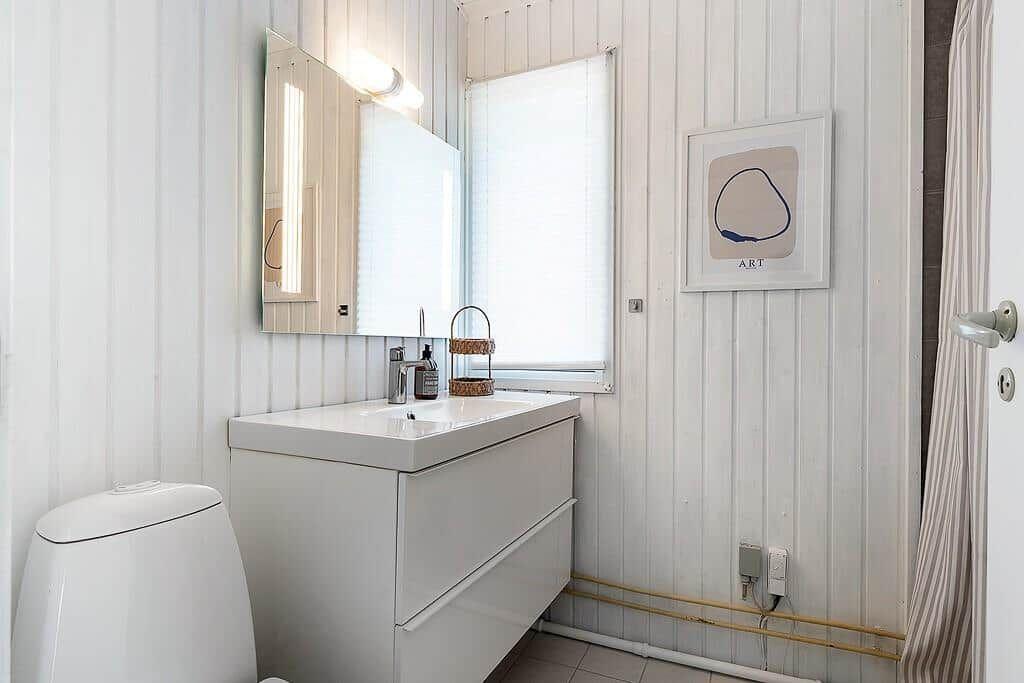 Bathroom with sink, mirror and toilet against white paneled walls.