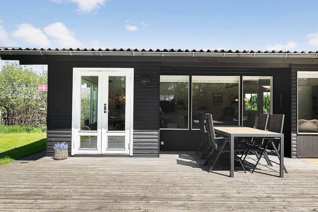 Modern villa with terrace, table and chairs. Large windows and white door.