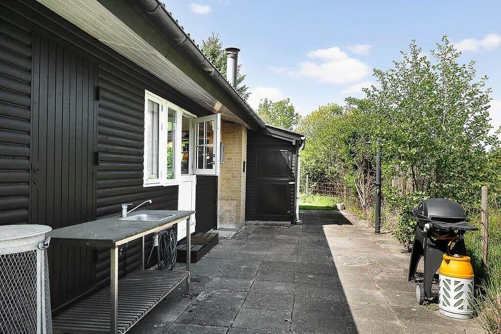 Outdoor area with grill, sink, and wooden house under blue sky.