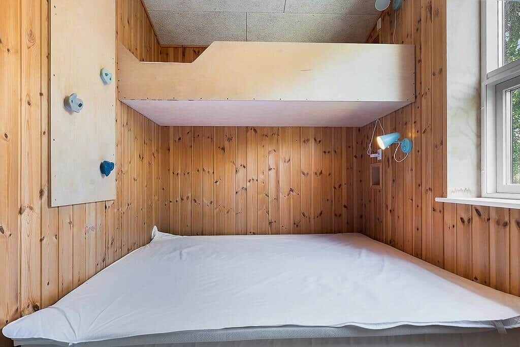 Room with wooden walls, lower bed, and upper bed with wall-mounted fixtures.