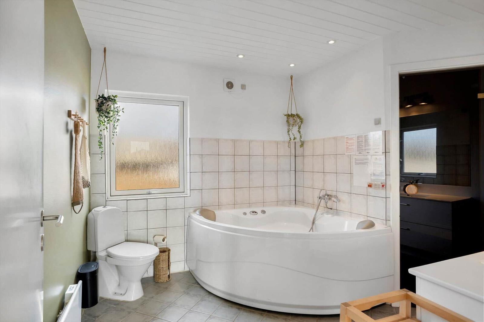 Bad mit Whirlpool, Toilette und Fenster mit getöntem Glas.