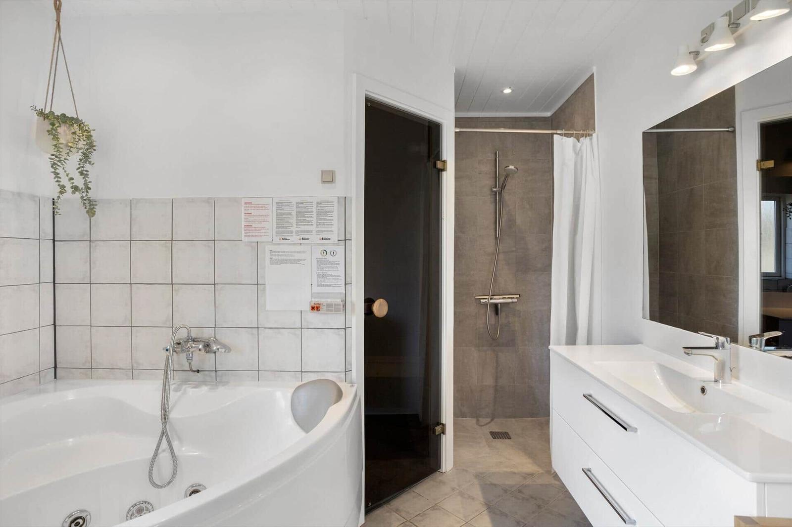 Badezimmer mit Badewanne, Dusche und Waschtisch. Weiße Fliesen und moderne Einrichtung.