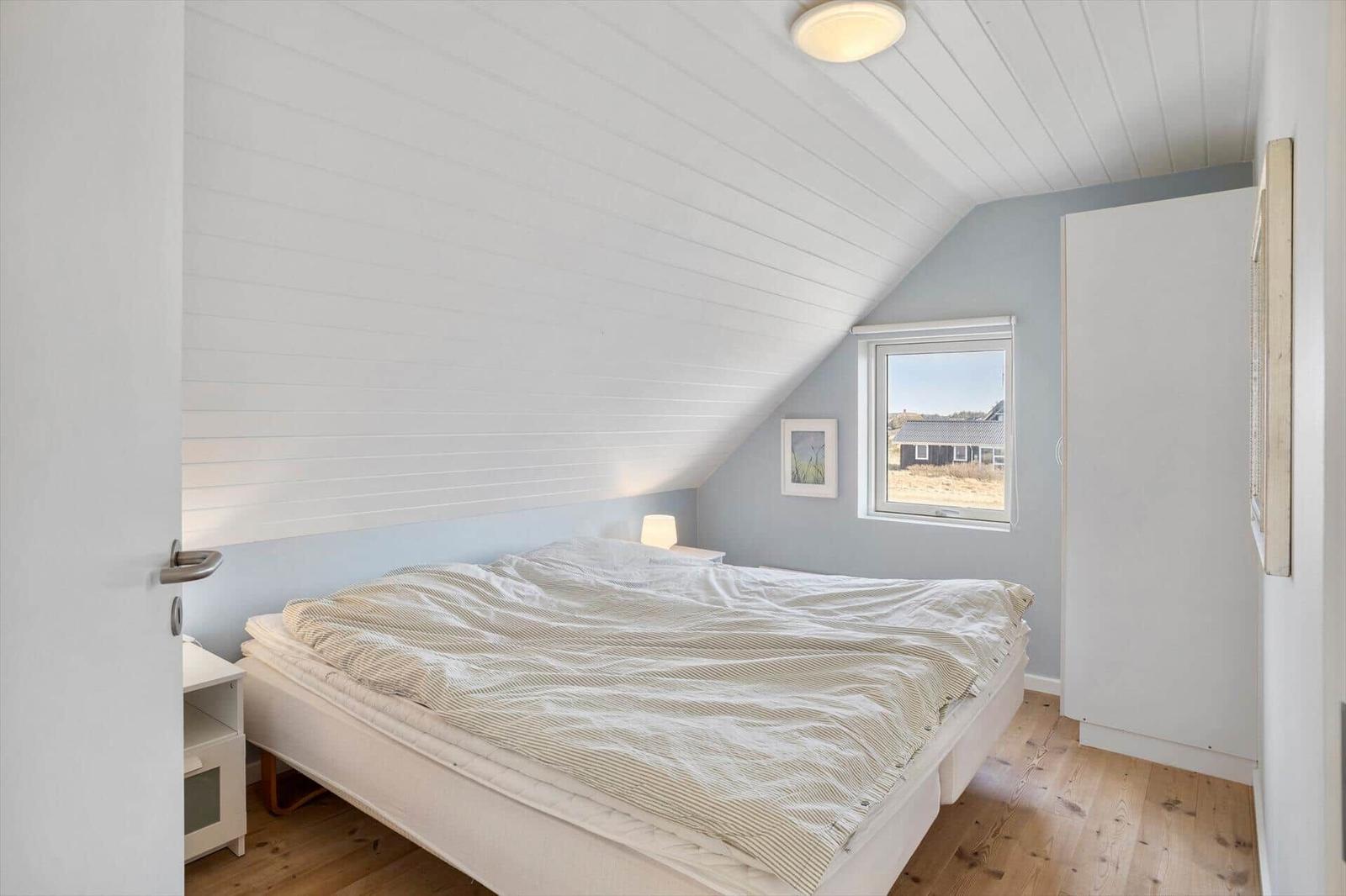 Schlafzimmer mit Dachschrägen, Bett, Fenster und Kleiderschrank.
