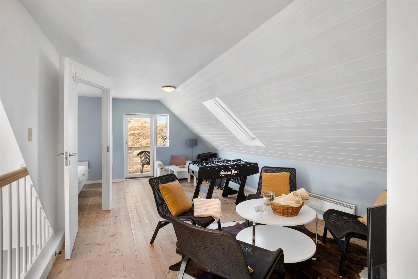 Dachgeschosswohnung mit Tischfußball, Sitzgelegenheiten und Blick auf Balkon.