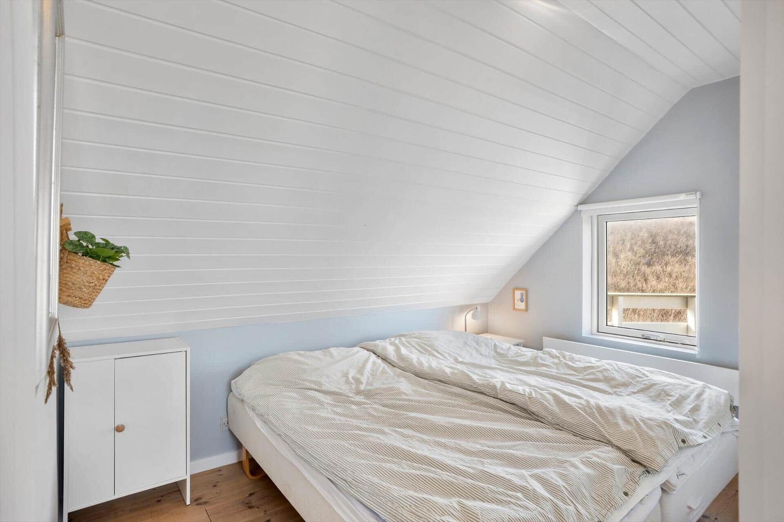 Schlafzimmer mit Dachschräge, Bett, kleinem Schrank und Fenster.