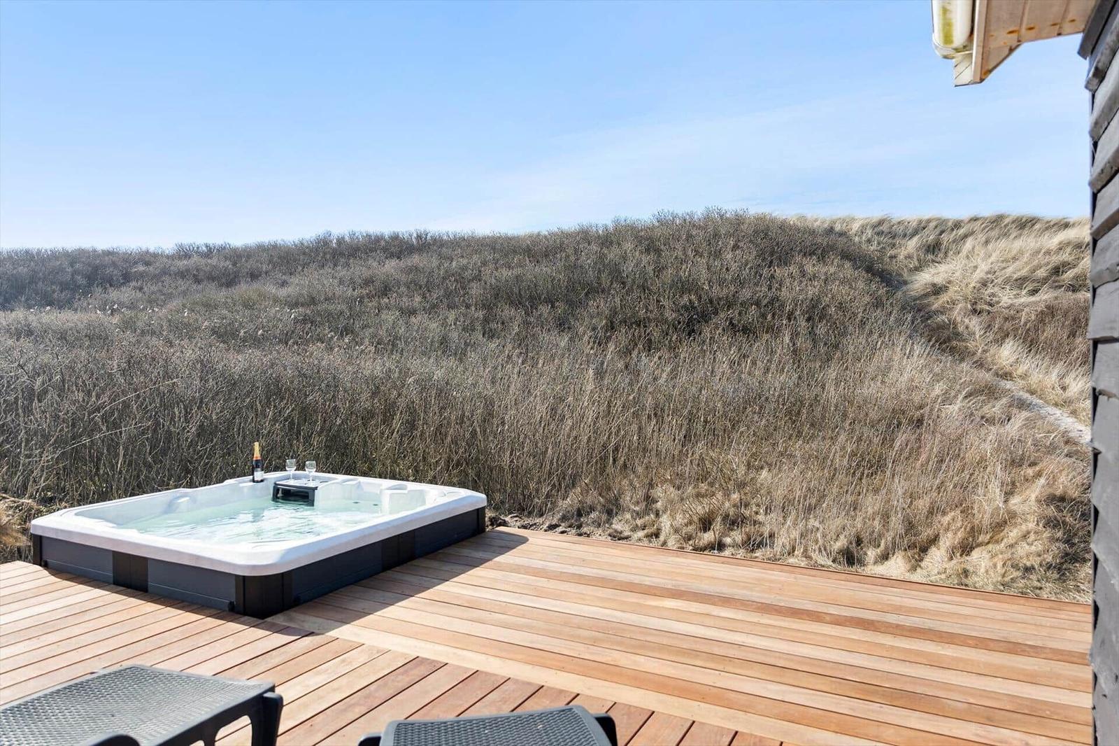 Hochwertige Whirlpool-Lounge auf Holzterrasse mit Blick auf Dünenlandschaft.