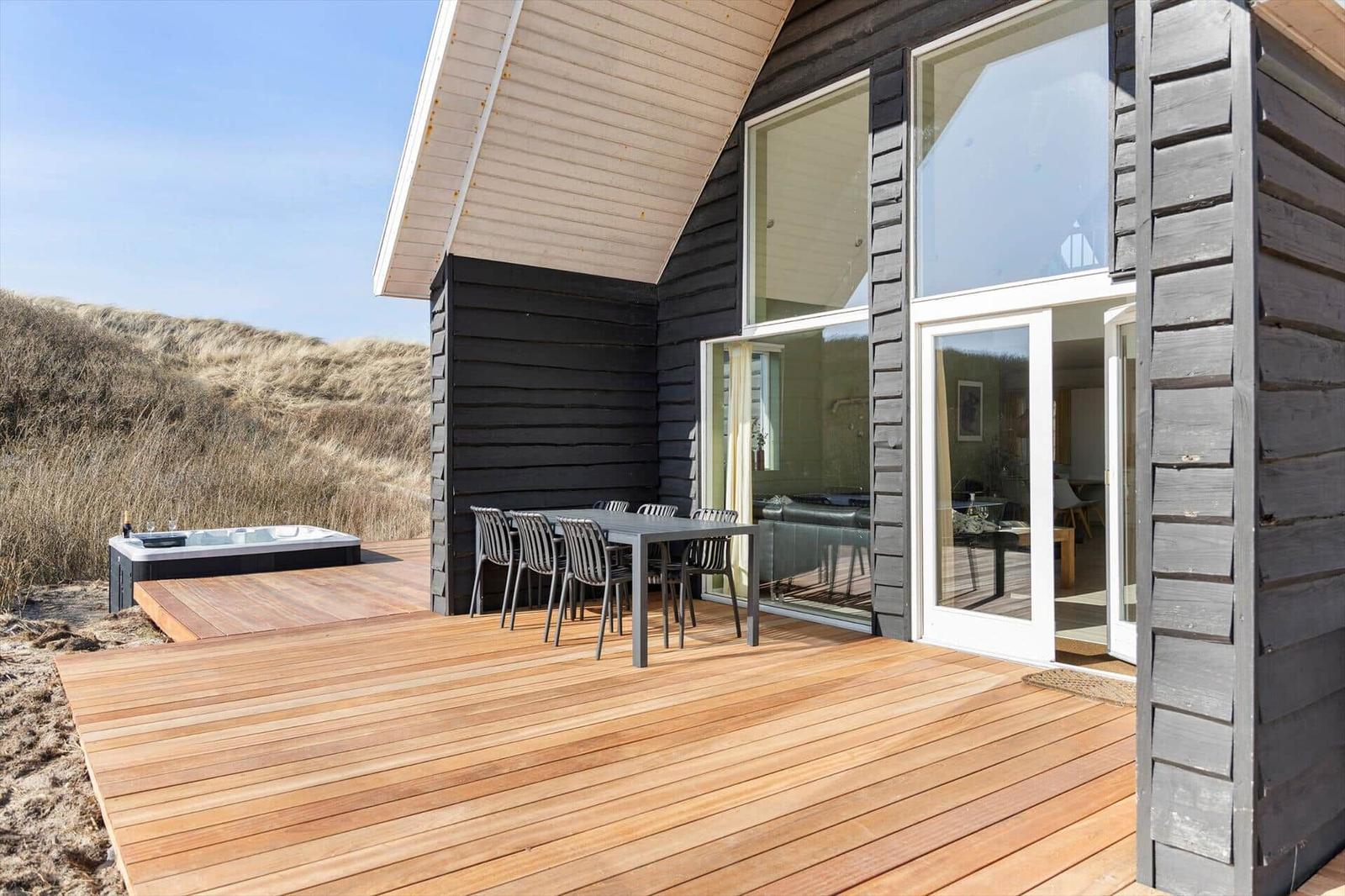 Terrasse mit Sitzgruppe und Whirlpool neben modernem Haus mit großem Fenster.
