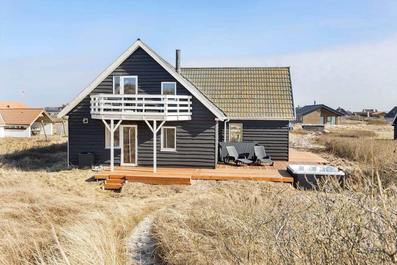 Holzhaus mit Balkon, Terrasse und Whirlpool in trockener Graslandschaft.