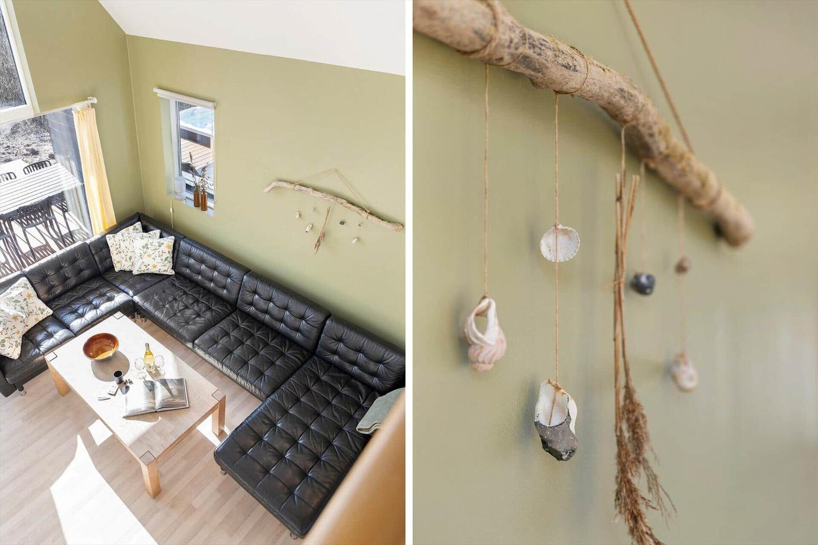 Schwarzes Ledersofa mit floralen Kissen und Wanddekoration aus Holz und Muscheln.