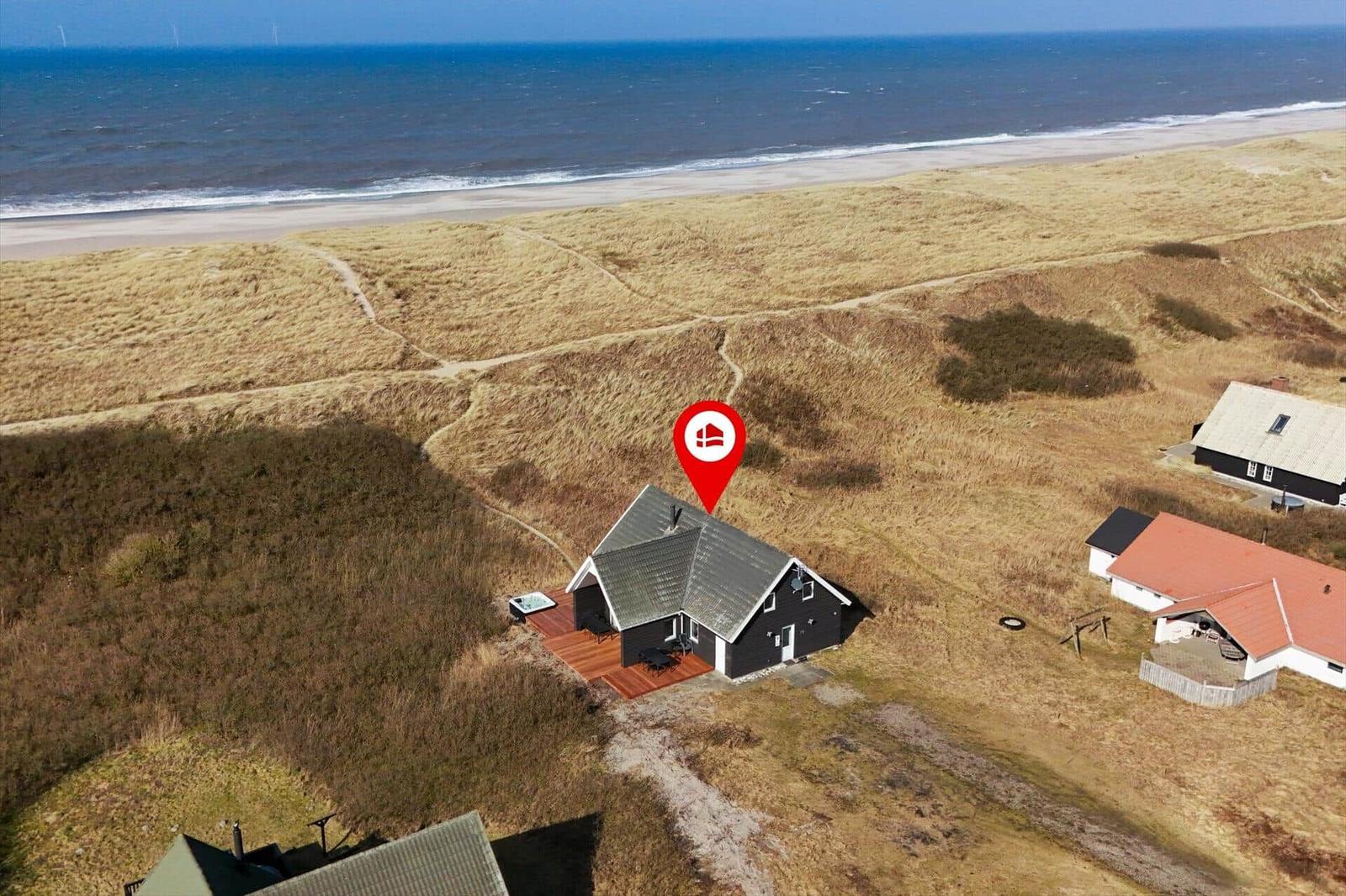Haus mit Terrasse an der Nordsee, umgeben von Dünen und Strand.