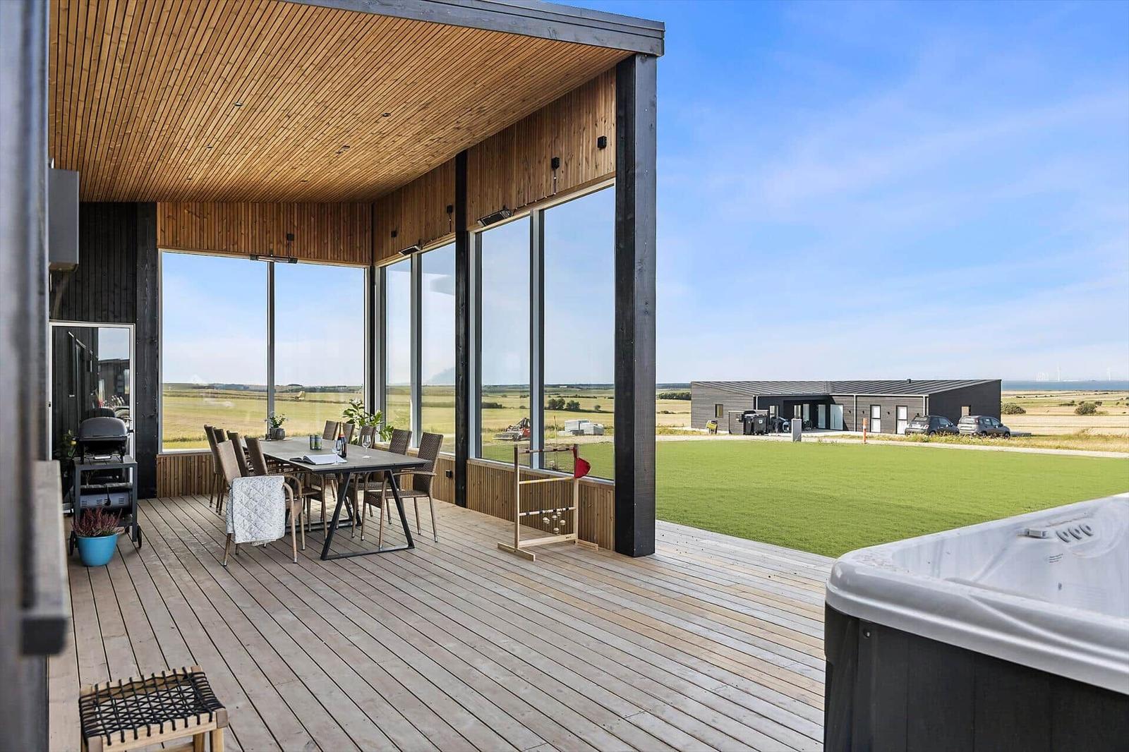 Terrasse mit Grill, Tisch und Sitzgelegenheiten. Blick auf grünes Feld und Nebengebäude.