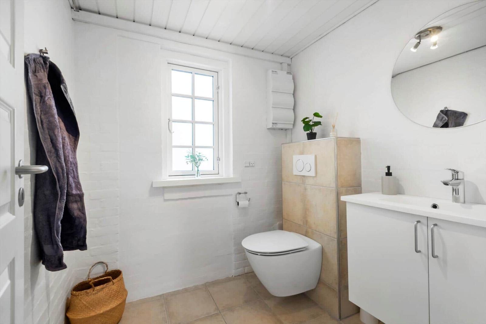Badezimmer mit Toilette, Waschbecken und Fenster. Wandheizung und Spiegel sind vorhanden.