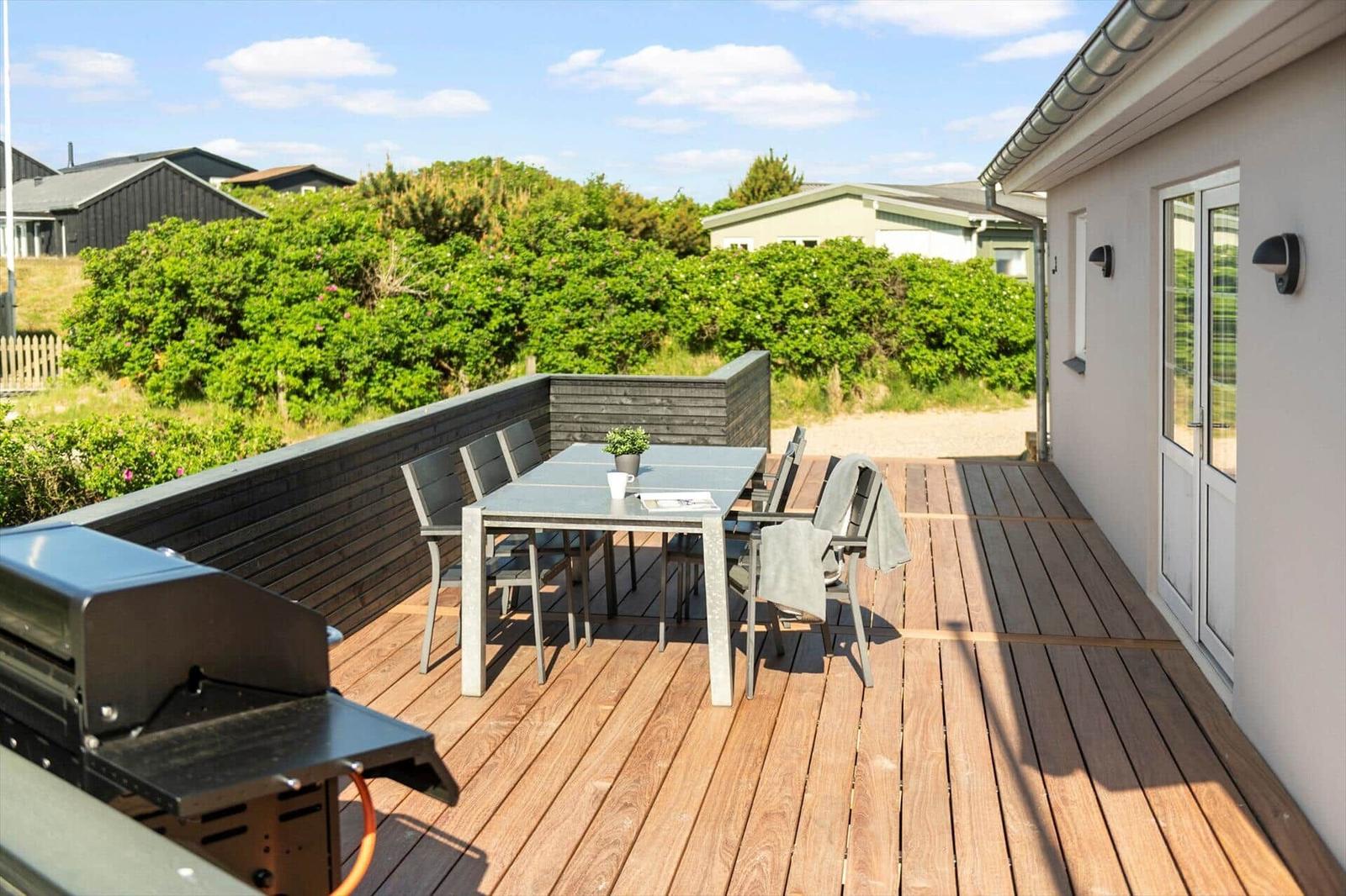 Deck with table, chairs, and grill. View of green hedge and houses.