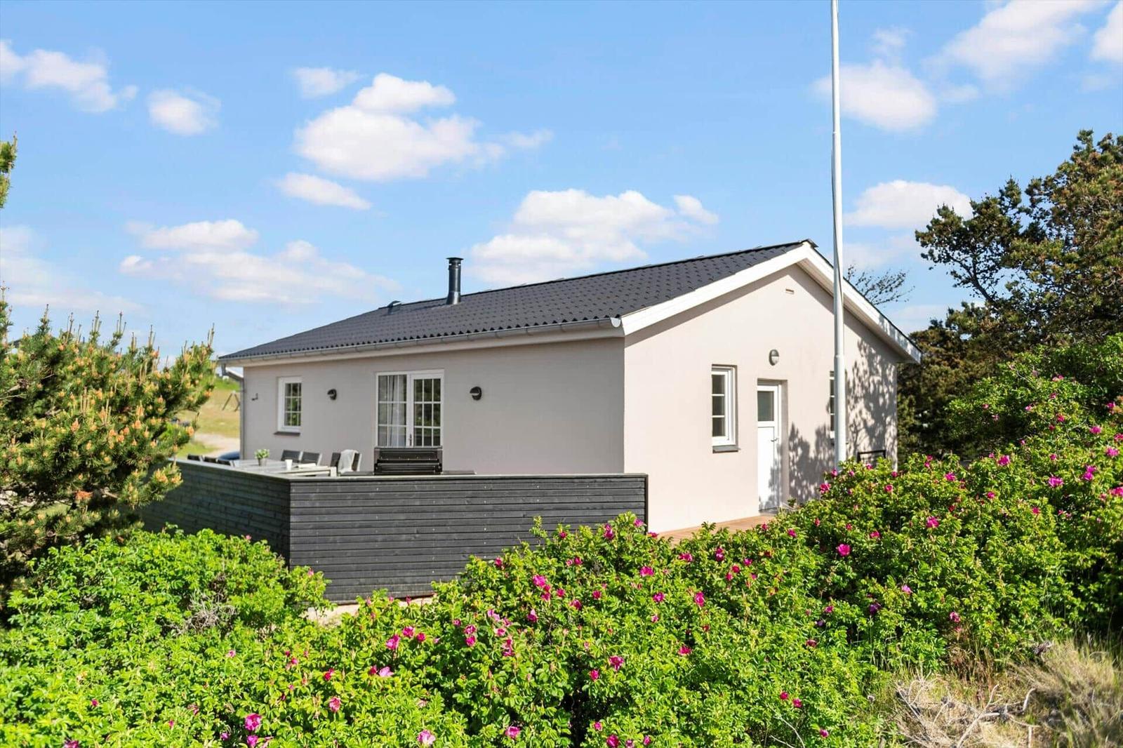 A light-colored house with a terrace and flower beds in the foreground.