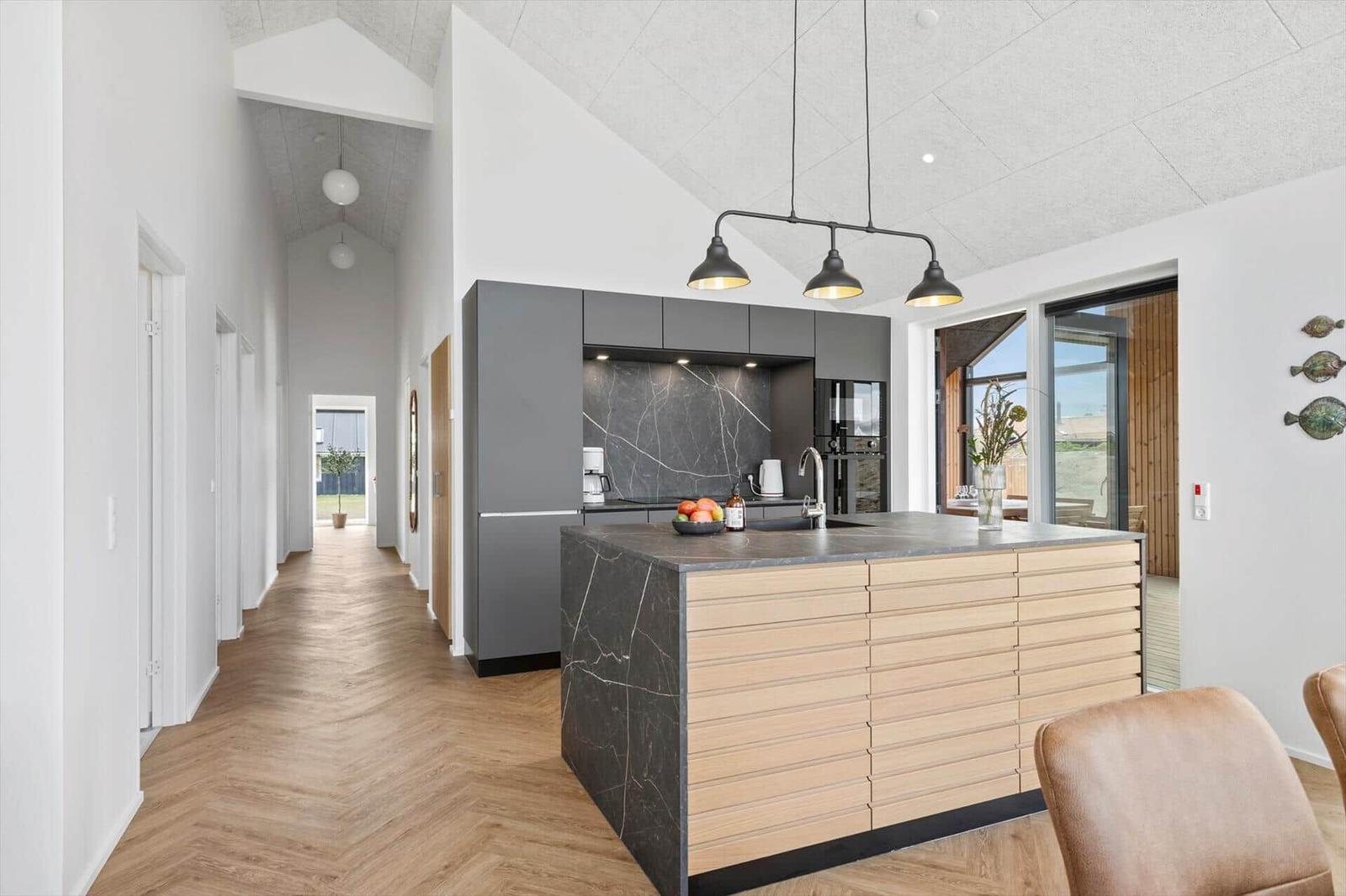 Moderne Küche mit Insel, dunkler Arbeitsplatte und Holzfronten. Helle Wände und Holzboden.