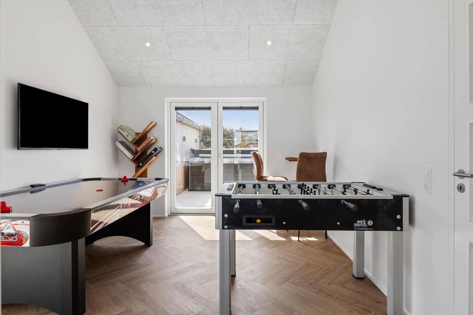 Raum mit Foosballtisch und Airhockeytisch, TV und Balkontür.