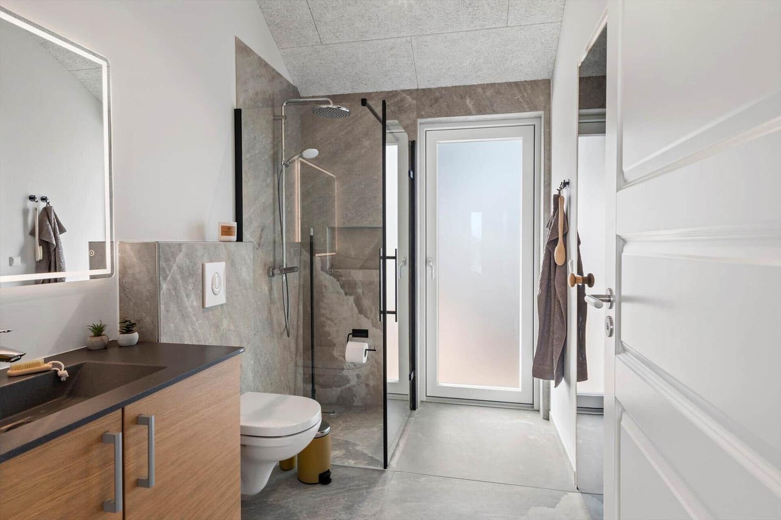 Badezimmer mit Dusche, Waschbecken und Toilette. Moderne Einrichtung mit Glaswand und Spiegelschrank.