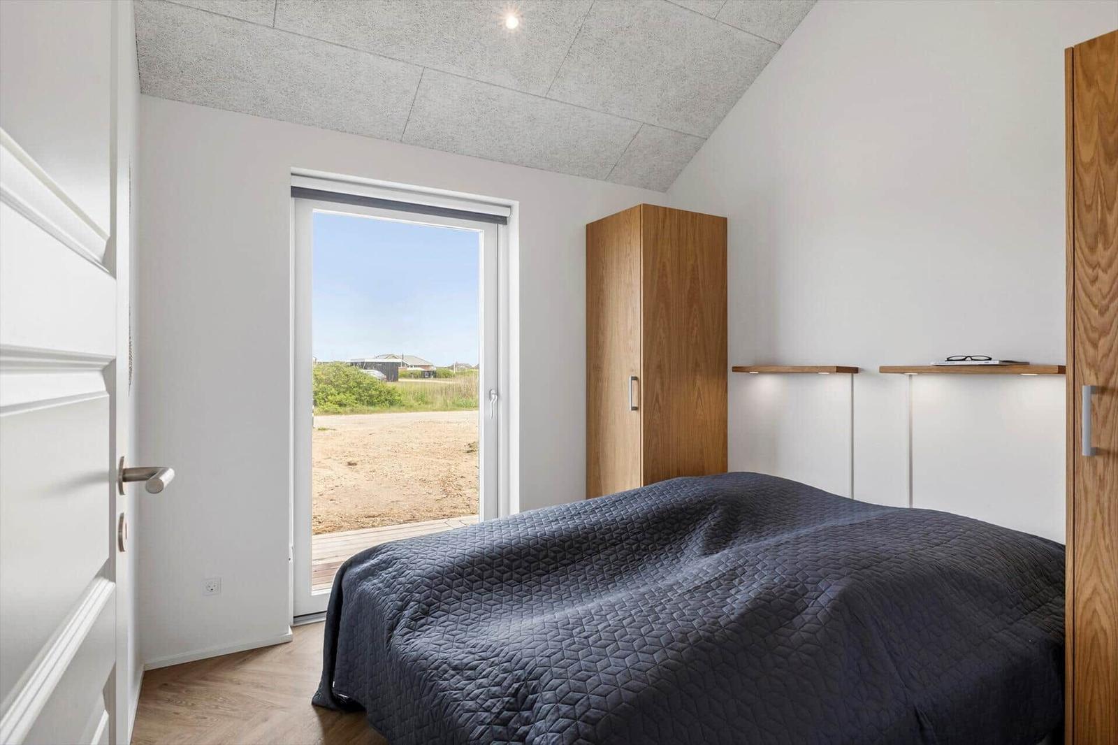 Schlafzimmer mit Bett, Schrank und Fenster zur Außenterrasse.