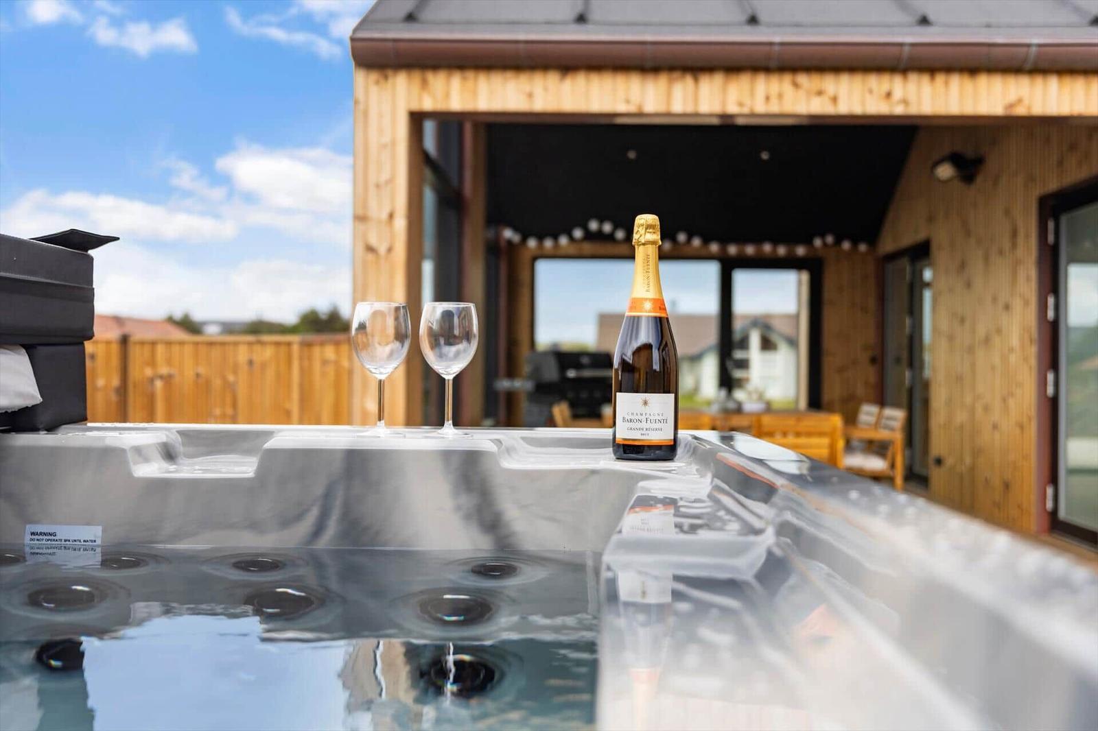 Hochwertiger Whirlpool mit Champagner und Gläsern auf einer Terrasse vor einem Holzhaus.