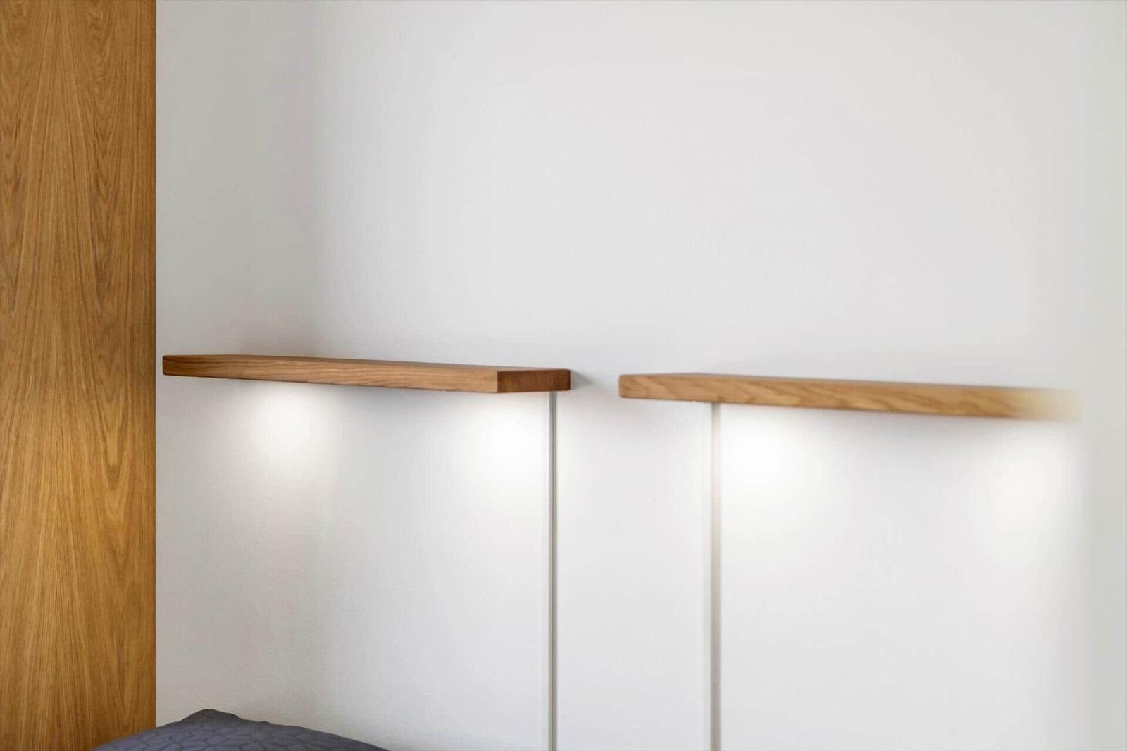 Zwei hölzerne Regale an der Wand über einem Bett mit integrierten Lichtern.
