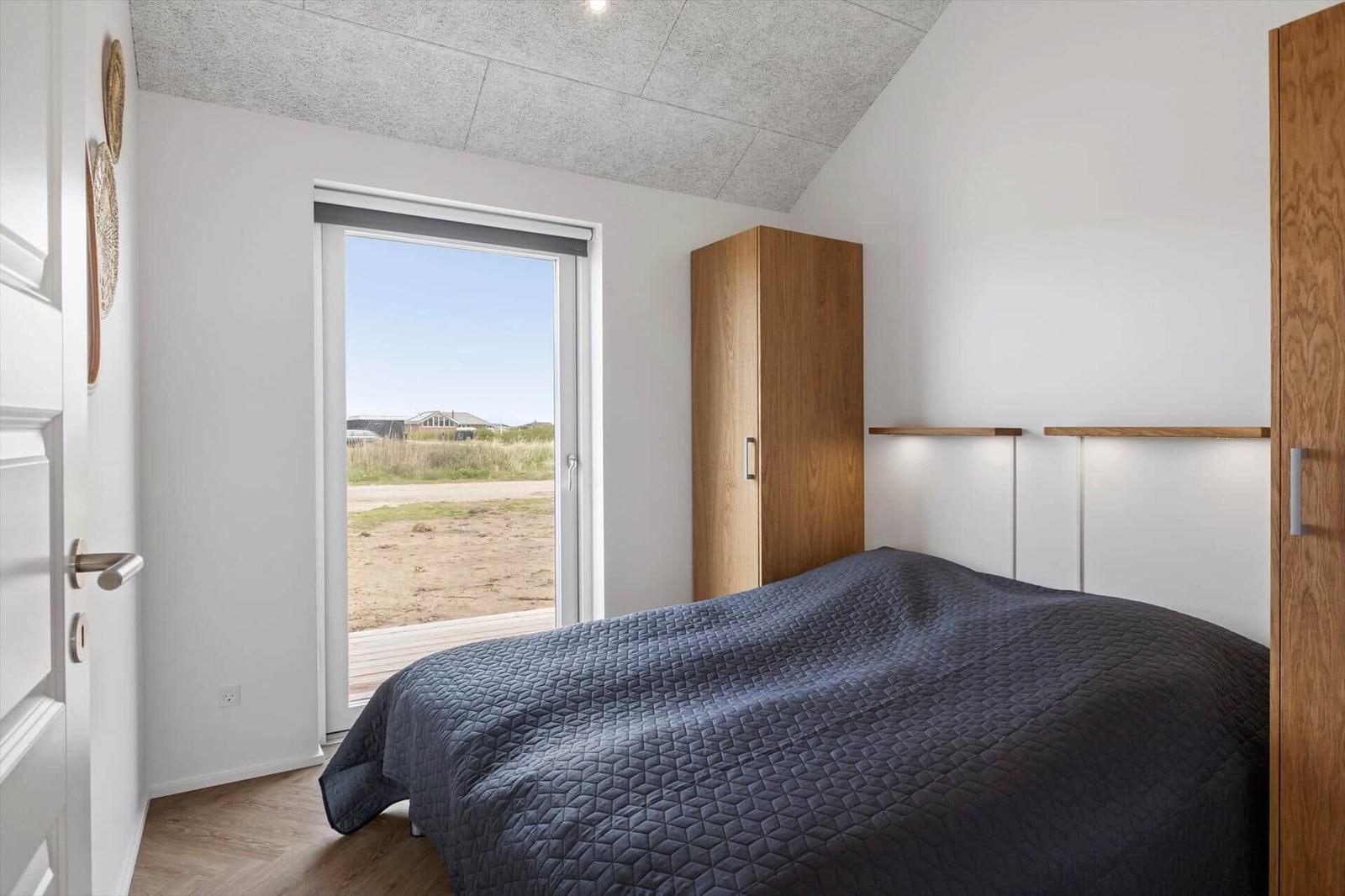 Schlafzimmer mit Bett, Kleiderschrank und Fensterblick auf Außenbereich.