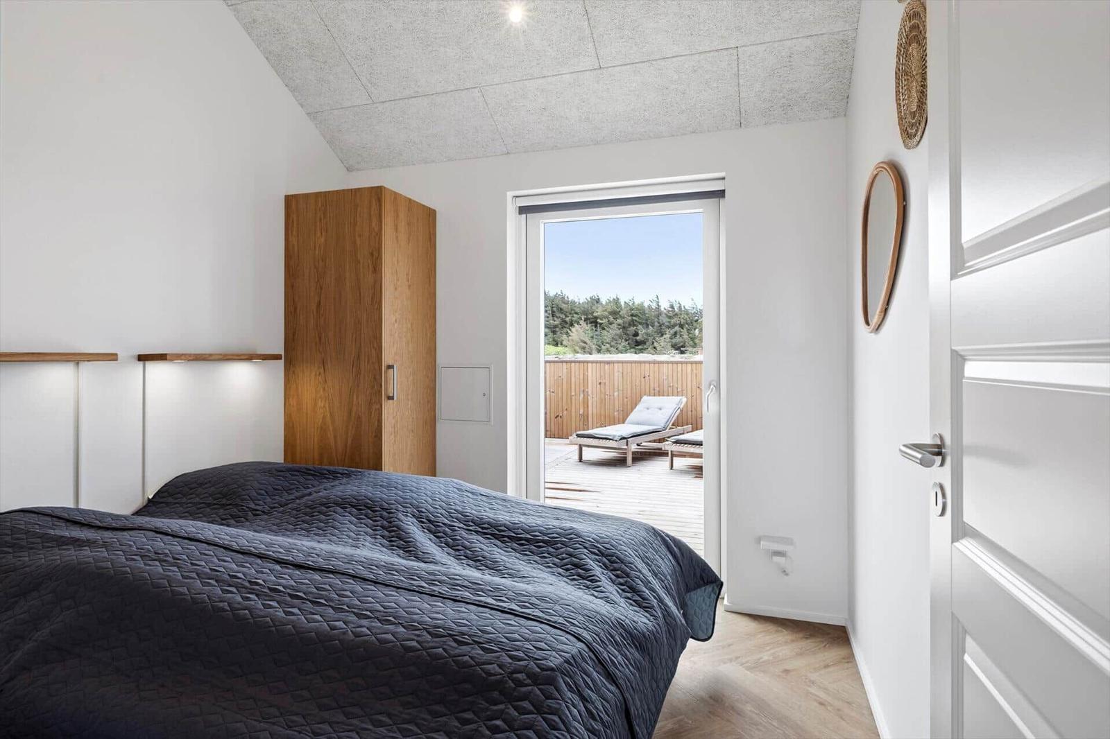 Schlafzimmer mit Balkon, Holzboden und Holzschrank. Blick auf Wald.