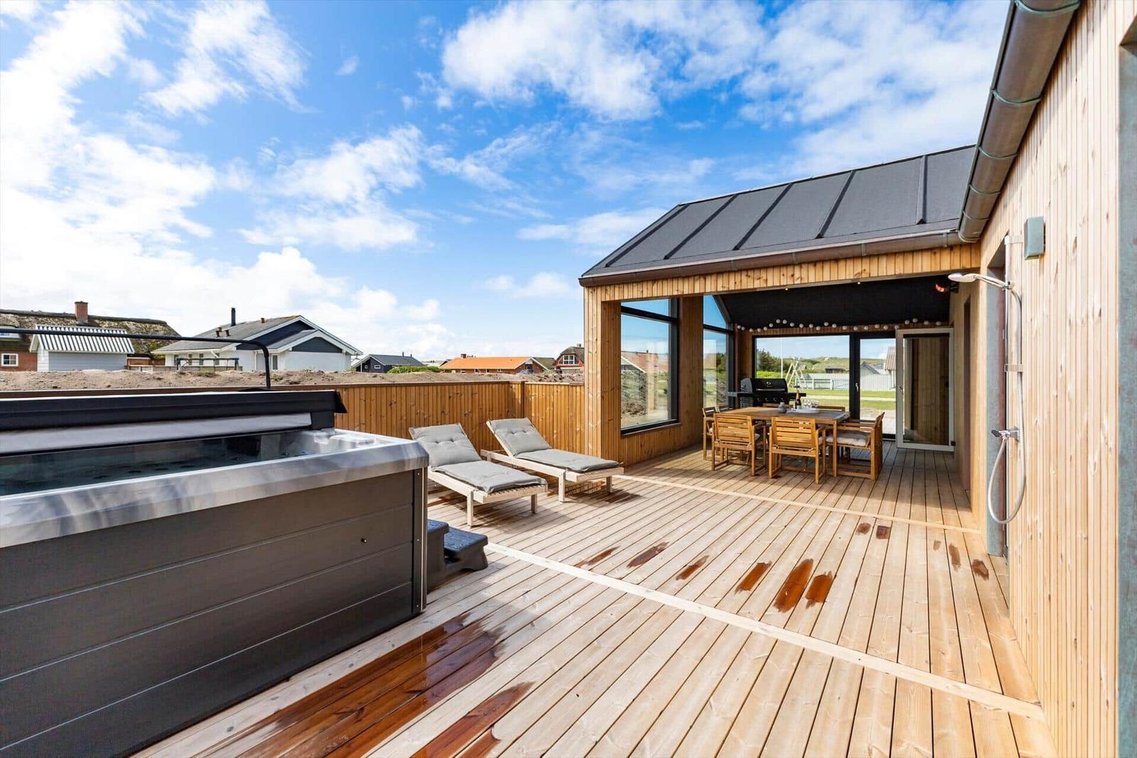 Terrasse mit Whirlpool, Liegestühlen und Grillbereich. Holzdeck und Sicht auf die Umgebung.