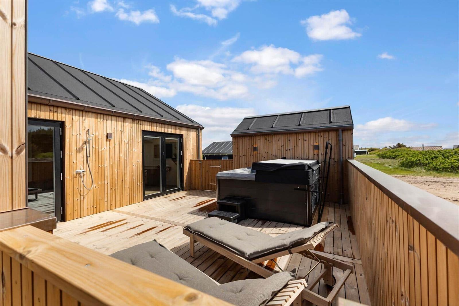 Holzterrasse mit Whirlpool, Liegen und Dusche. Blick auf grüne Landschaft.