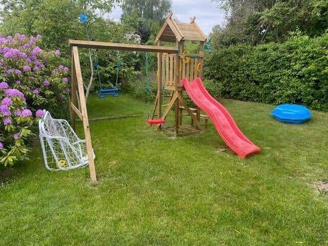 Backyard with playground, slide, and swing. Lawn and flower bed.