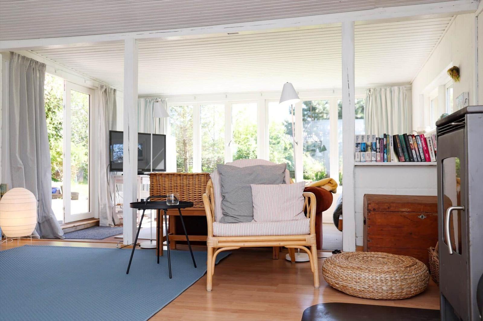 Wohnzimmer mit Sessel, Teppich und Bücherregal. Große Fenster mit Blick auf Garten.