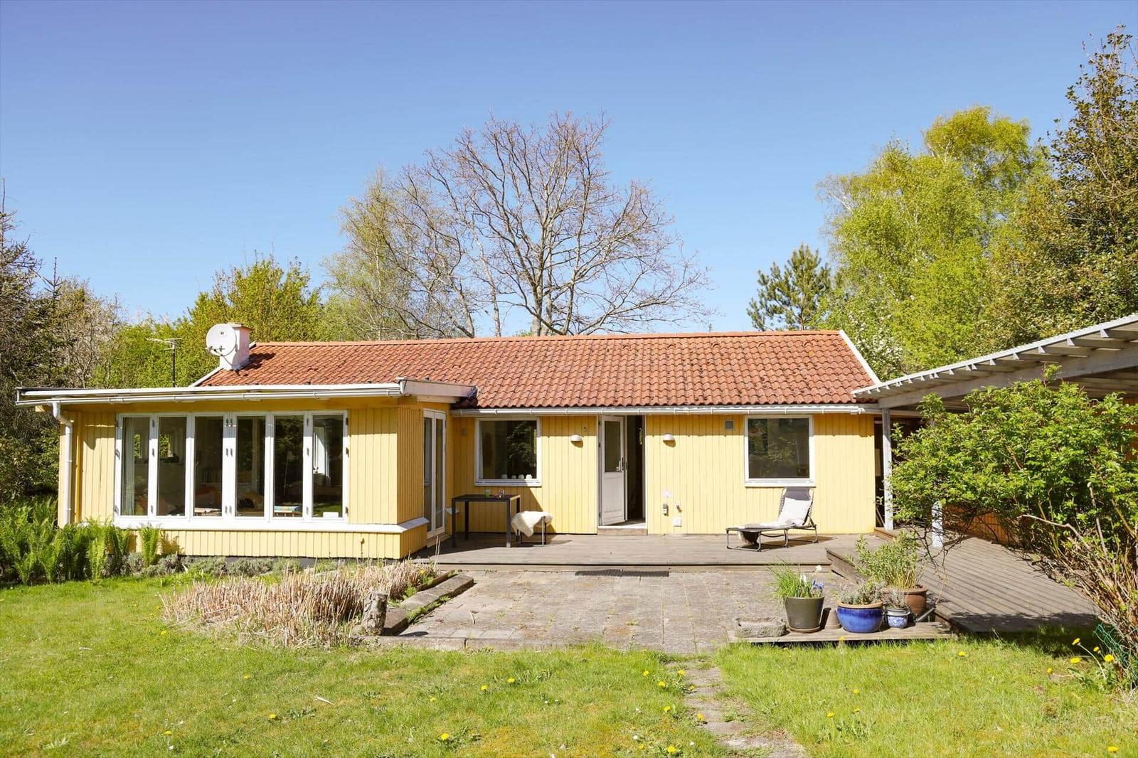 Ein gelbes Haus mit Terrasse und Garten. Dachziegel, Fenster und Pflanzen sind sichtbar.