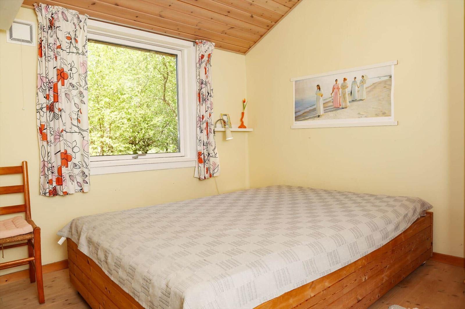 Schlafzimmer mit Holzbett, Fenster mit Blumenvorhängen und Wandbild.