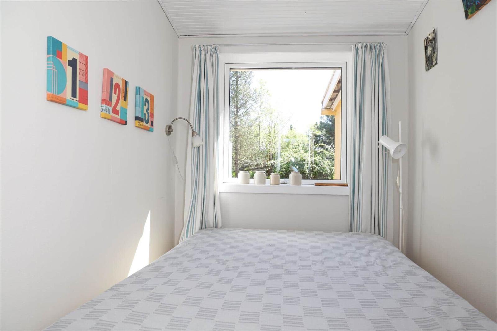Schlafzimmer mit Bett, Fenster und Wandbildern.