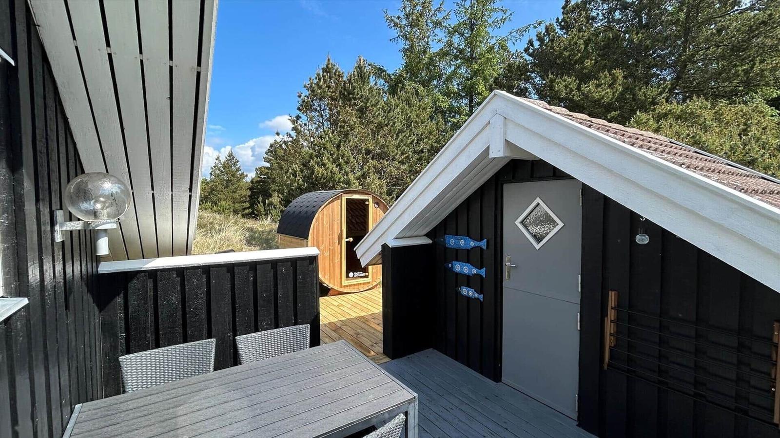 Terrasse mit Tisch und Stühlen, Sauna und kleines Haus mit Tür.