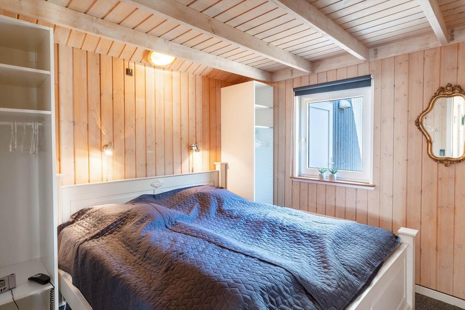 Schlafzimmer mit Holzwand, weißem Bett und Fenster mit Pflanzen.