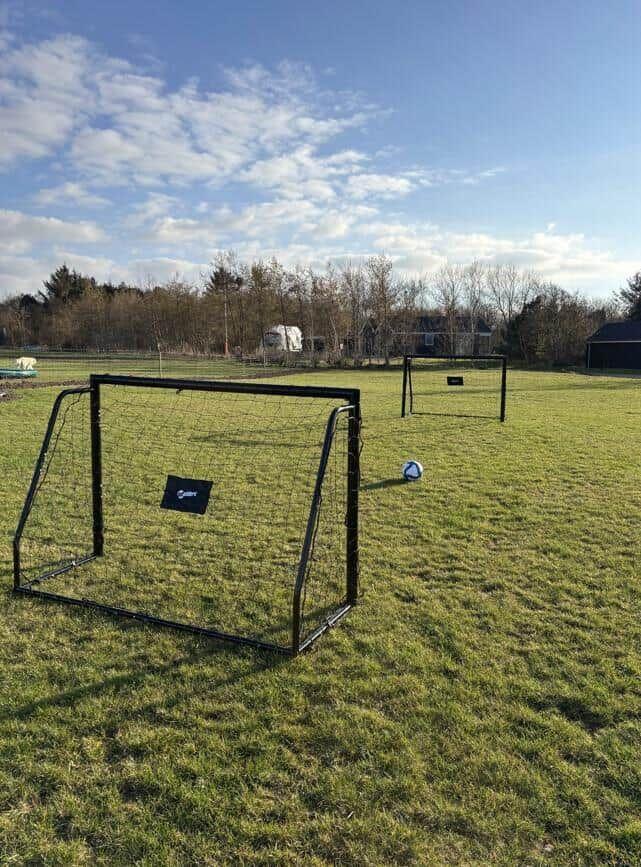 Zwei Fußballtore und ein Ball auf einem grünen Rasenfeld unter blauem Himmel.