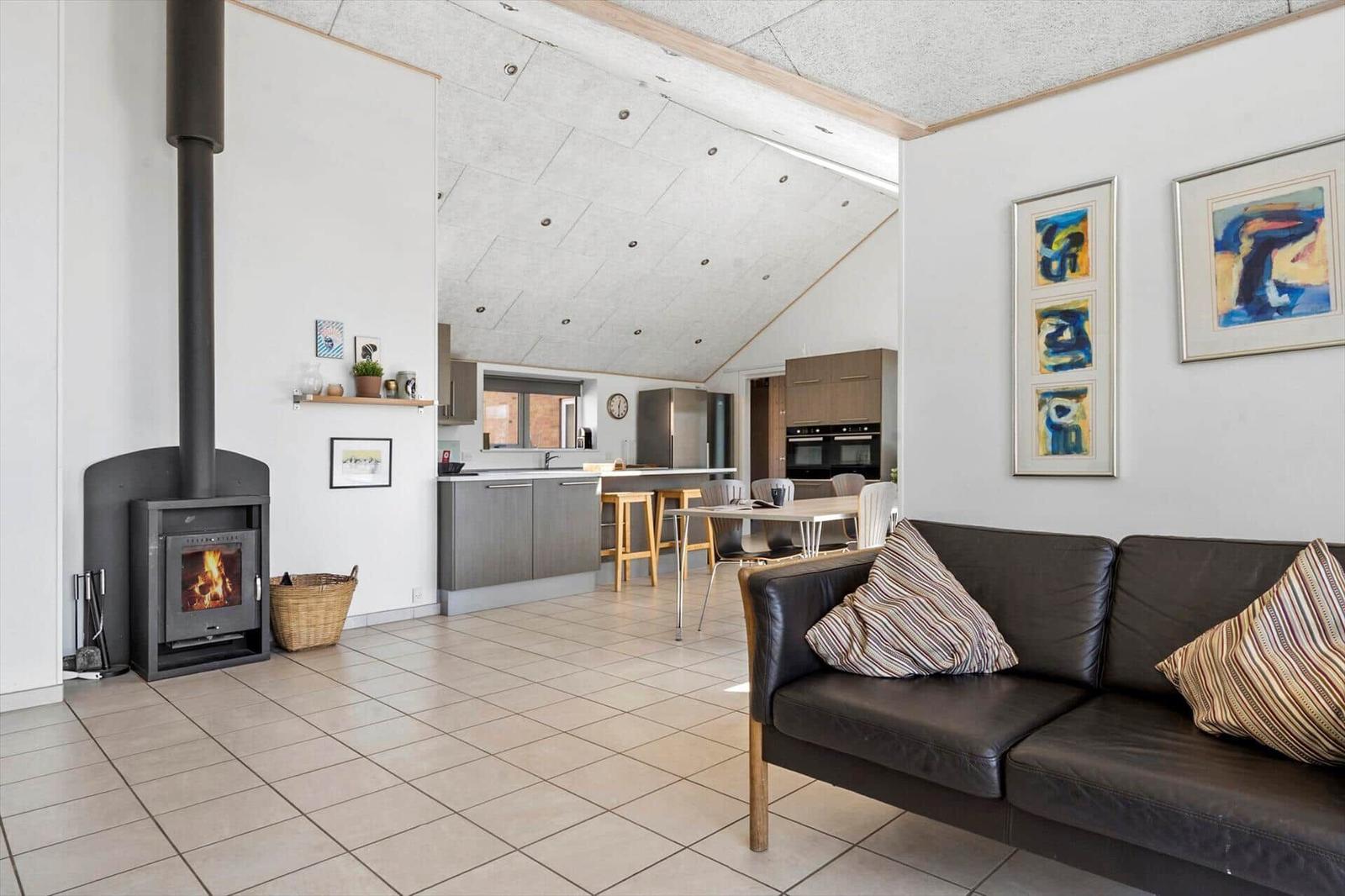Wohnbereich mit Sofa, Kamin und offener Küche unter schrägem Dach.