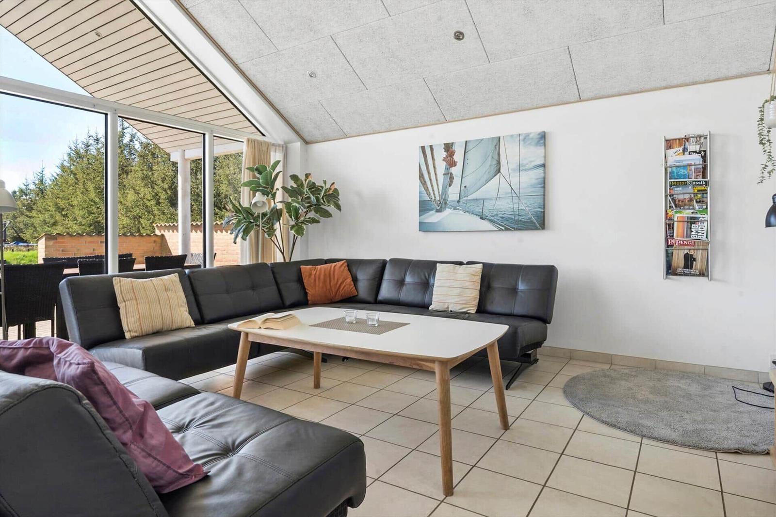 Lichter Raum mit Sofa, Tisch und Wandbild. Große Fenster und Pflanzen.