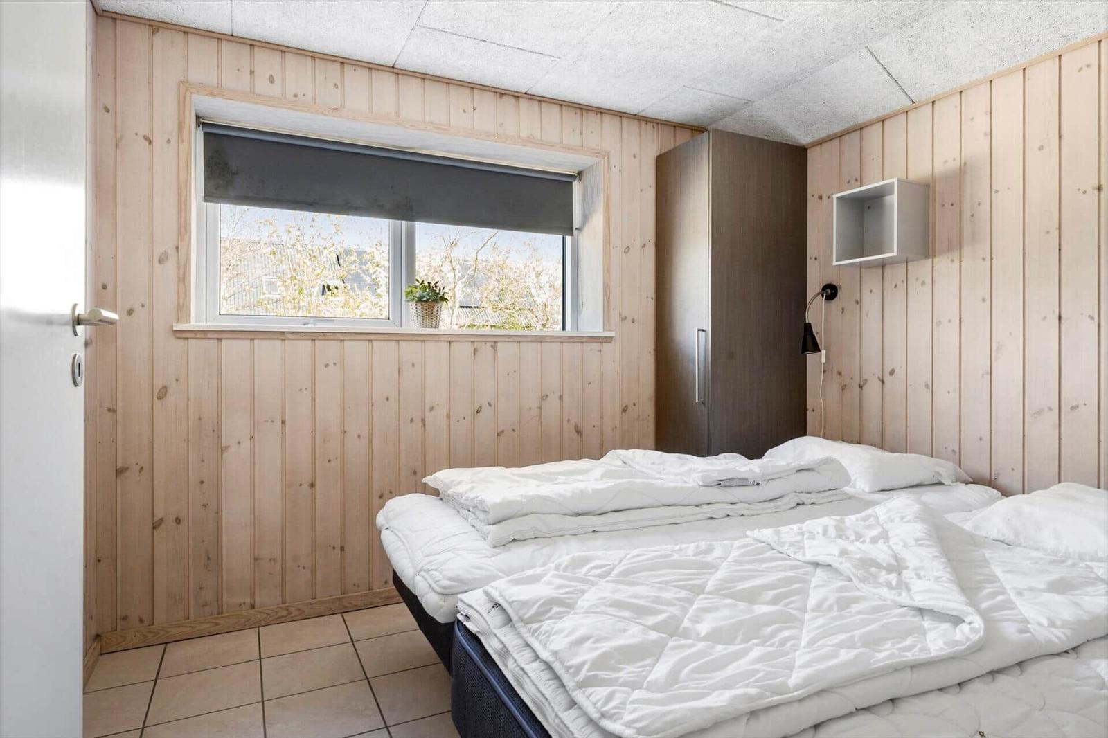 Schlafzimmer mit Holzwand, Bett, Fenster und Schrank.
