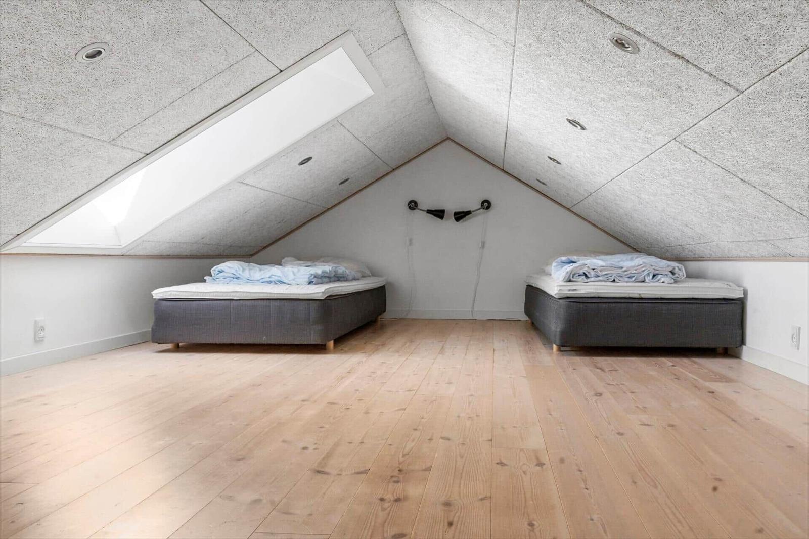 Zwei Betten in einem Dachgeschosszimmer mit Holzboden und Dachfenster.