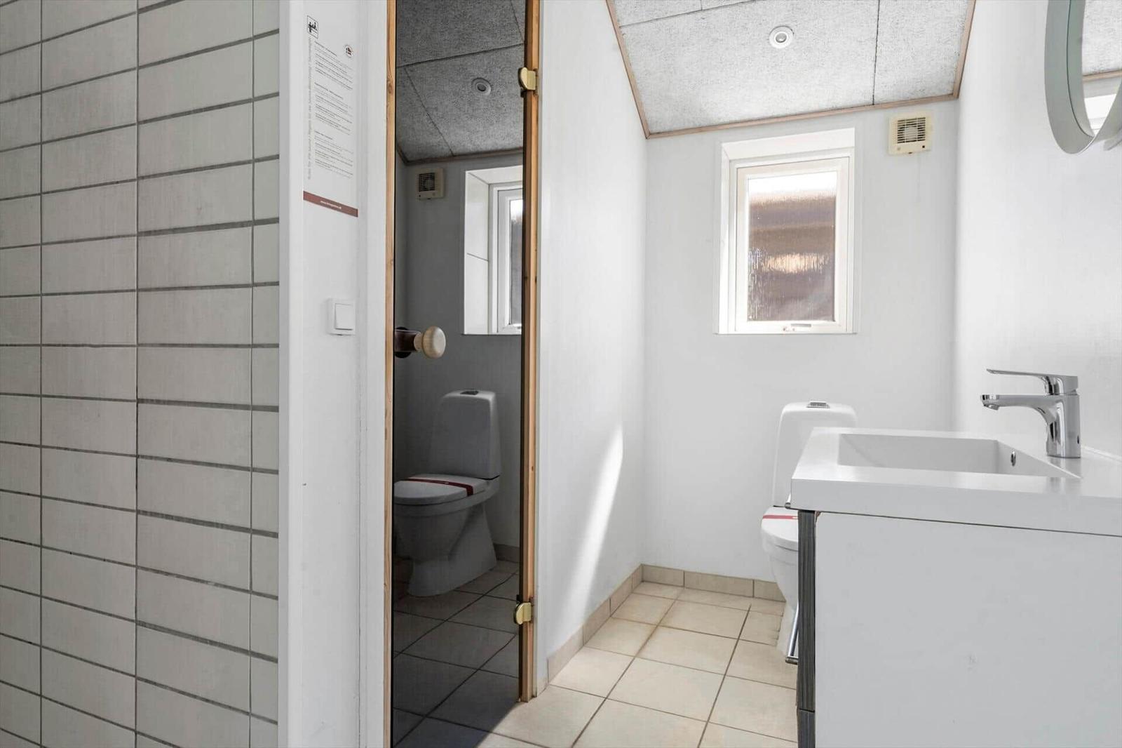 Badezimmer mit Waschbecken, Toilette und Dusche. Fenster und weiße Wände.