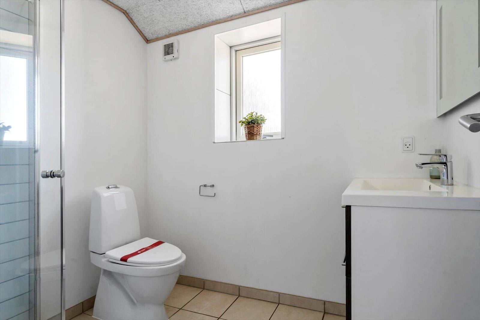 Badezimmer mit Toilette, Waschbecken und Dusche. Fenster mit Pflanze.